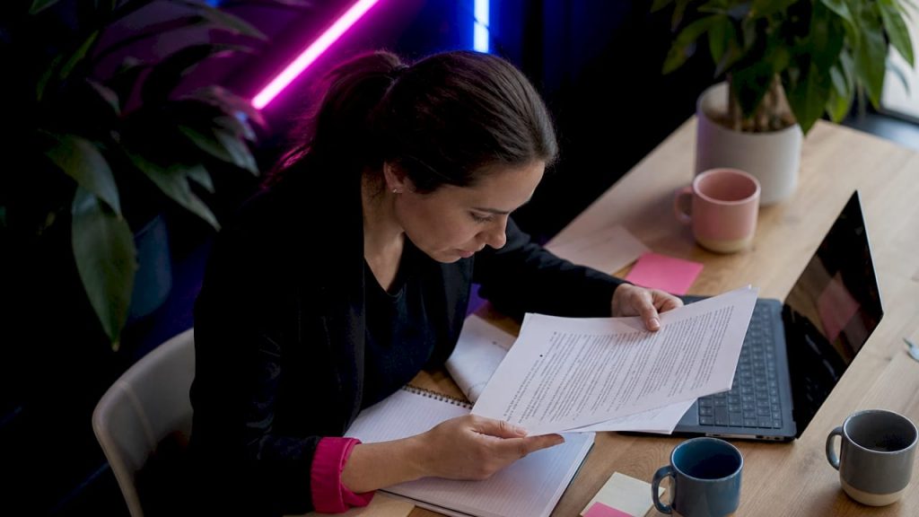 1782708188713womanreviewingprintedwebsecurityguide | Webstart Une femme parcourt attentivement un guide imprimé sur la sécurité en ligne.