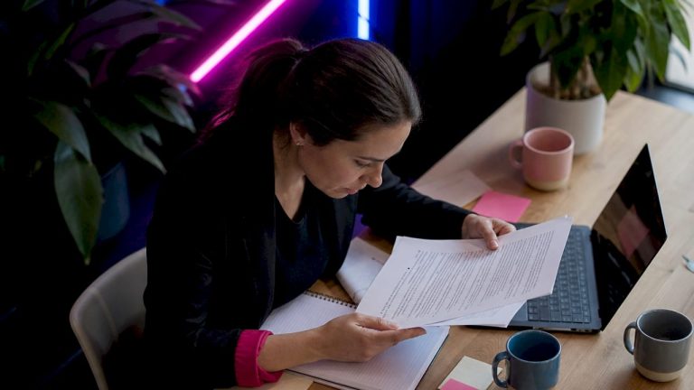1782708188713womanreviewingprintedwebsecurityguide | Webstart Une femme parcourt attentivement un guide imprimé sur la sécurité en ligne.