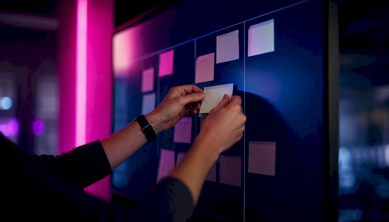 Des mains ajoutent une nouvelle tâche sur un tableau Kanban.